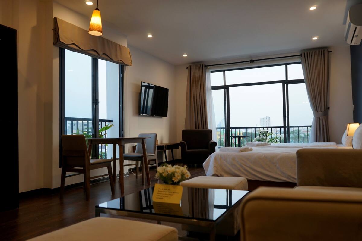 A hotel room with a bed, a desk with a chair, a TV, and a balcony with a view.
