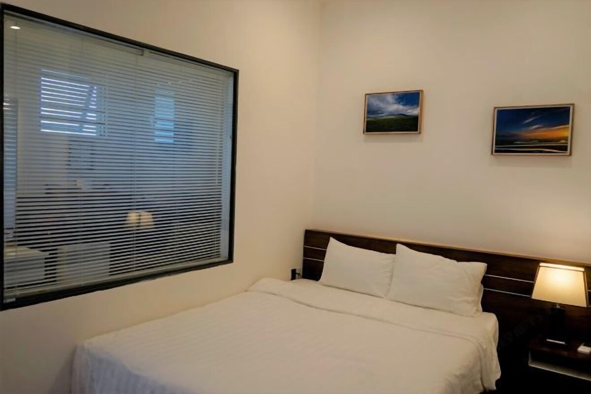 A hotel room with a bed, a nightstand, a lamp, and two framed pictures on the wall.