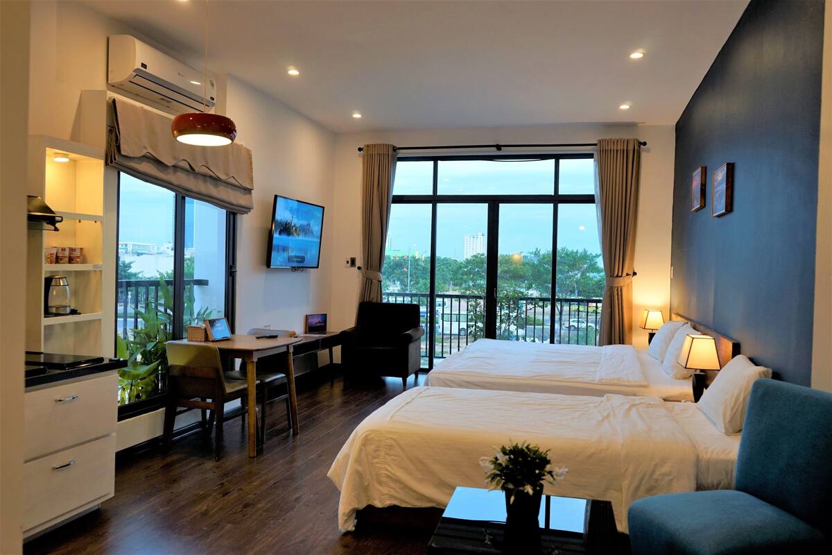A hotel room with two beds, a desk, a chair, a TV, and a balcony with a view.