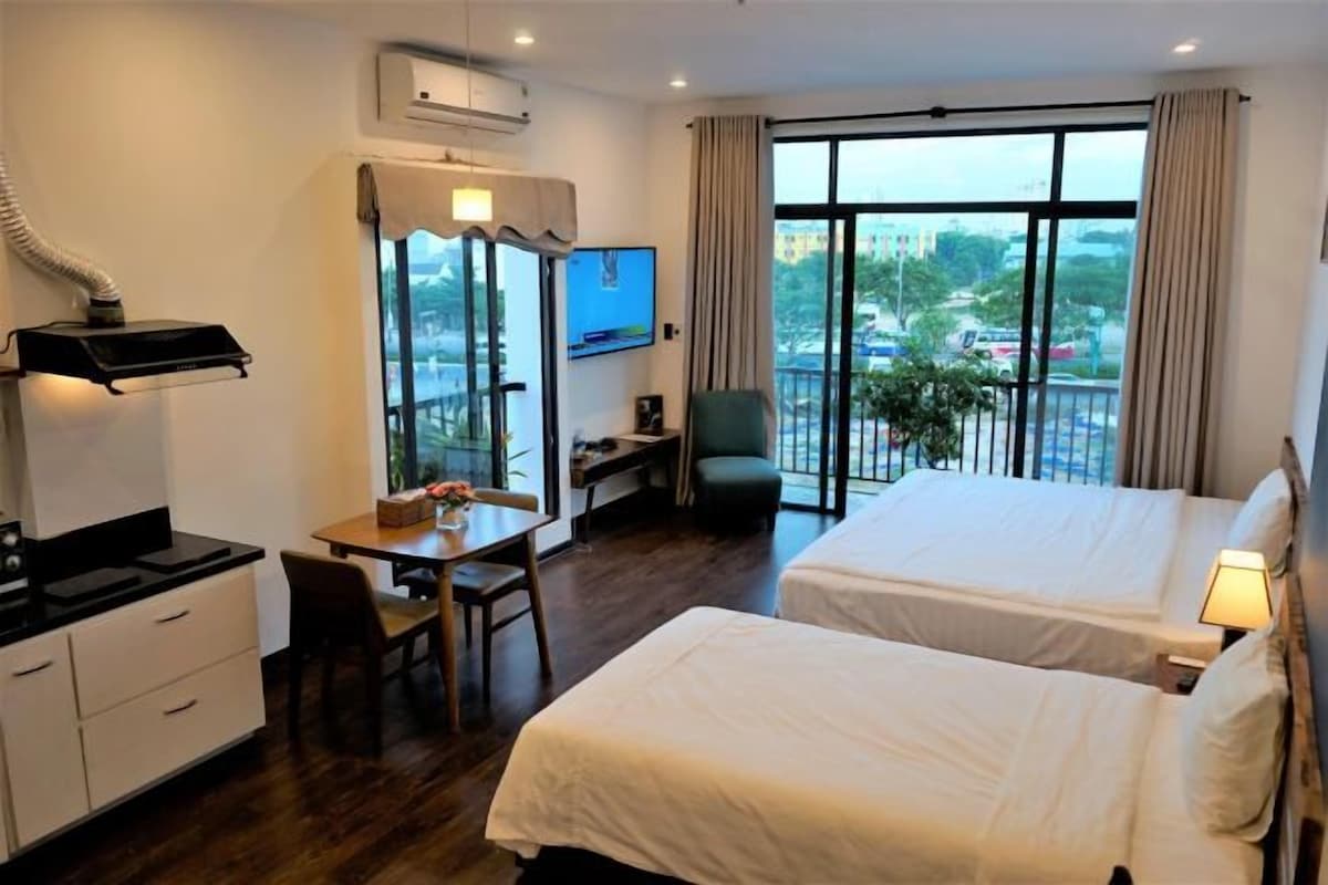A hotel room with two beds, a desk with a chair, a TV, and a large window with a view.