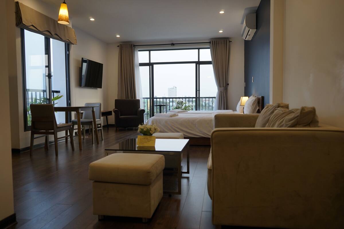 A hotel room with a bed, two sofas, a coffee table, a TV, and a balcony with a view.