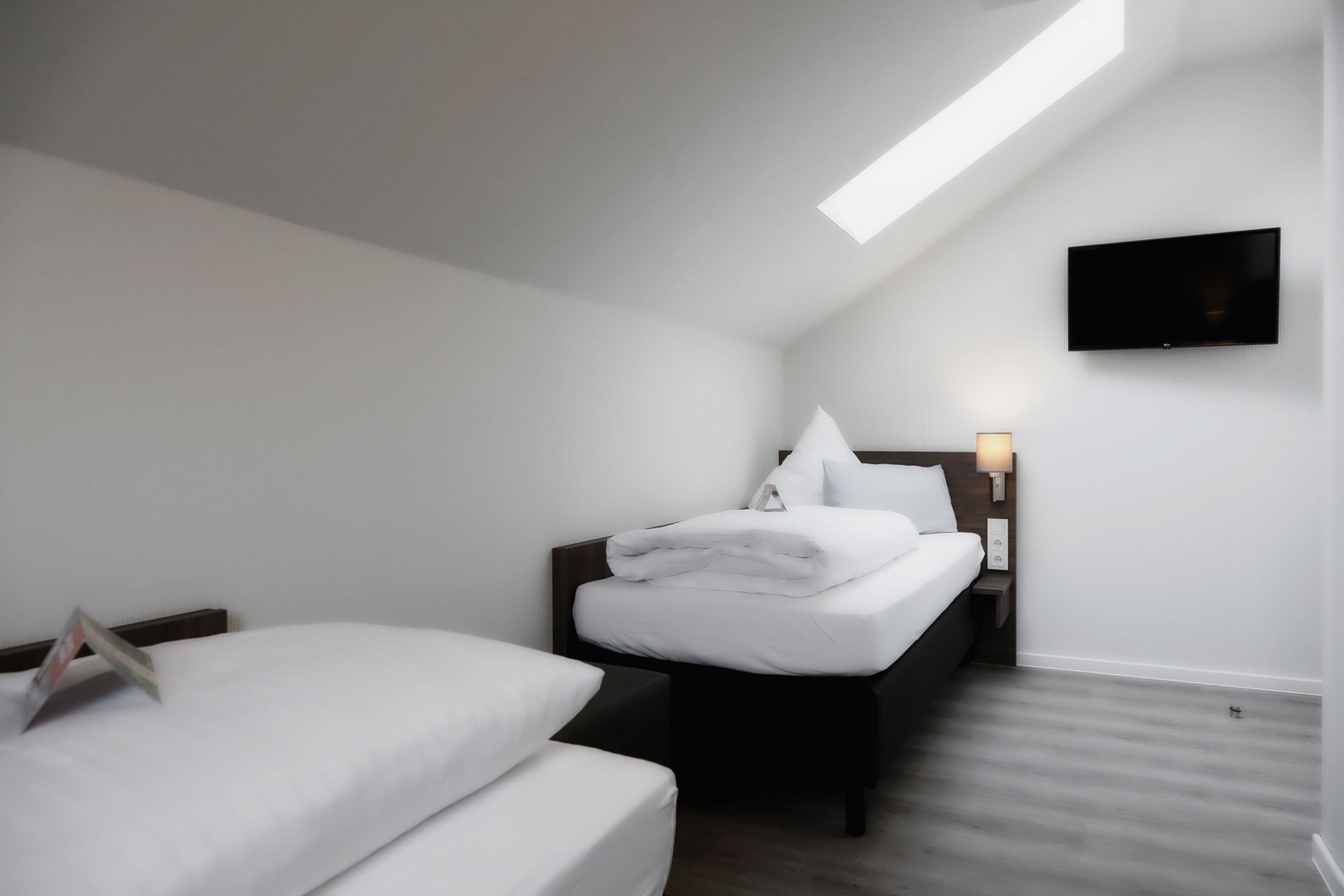 A modern hotel room with a bed, bedside table, and a mounted TV.