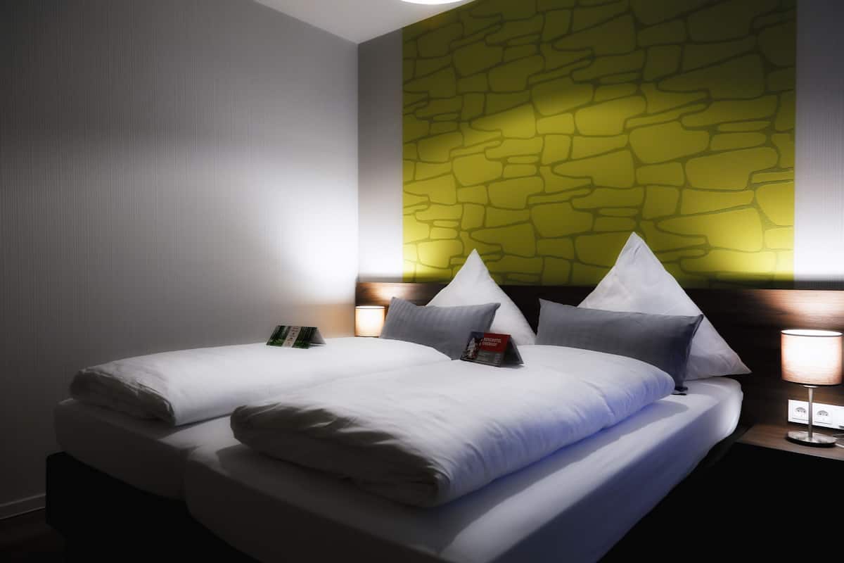 A hotel room with a bed, pillows, a nightstand, and a wall with a textured pattern.
