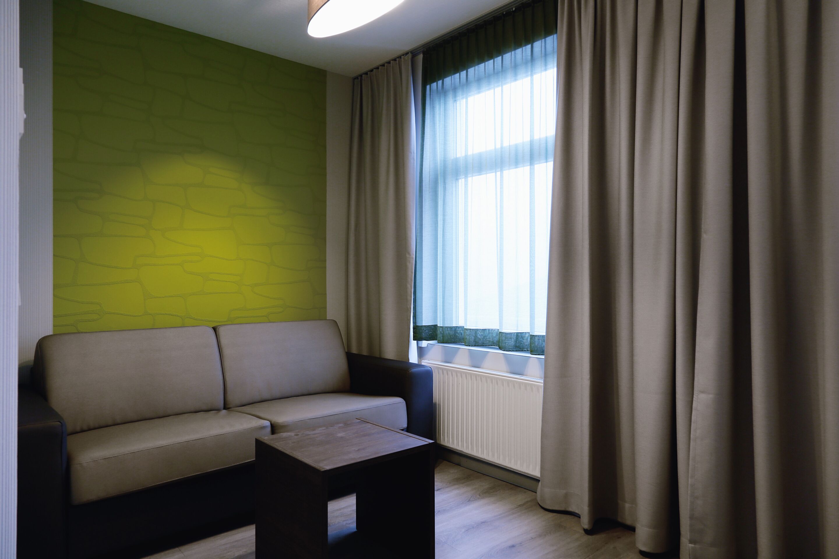 A modern living room with a sofa, a small table, a radiator, and a window with curtains.