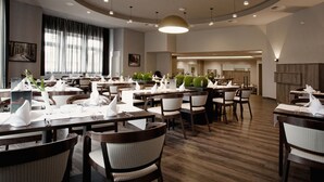 Ein geräumiges Restaurant mit mehreren Esstischen, Stühlen und einem großen Fenster mit Vorhängen.