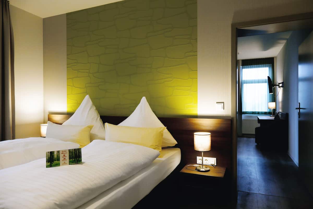 A hotel room with a large bed, a nightstand with a lamp, and a wall with a stone-like pattern.