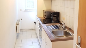 A compact kitchen with white cabinets, a built-in oven, a coffee maker, and a window with a view of greenery. - City Apartment 5-6 Personen (Hannover)