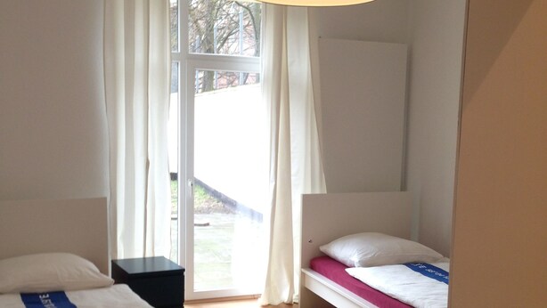 A bedroom with two beds, a window with curtains, a wooden floor, and a hanging light fixture. - City Apartment 5-6 Personen (Hannover)