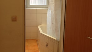 A bathroom with a bathtub, a window with a curtain, and tiled walls. - City Apartment 5-6 Personen (Hannover)