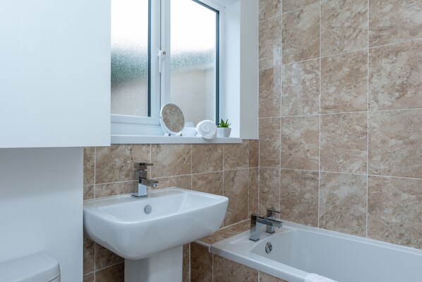Un baño con lavamanos blanco, espejo, bañera y ventana con vidrio esmerilado.