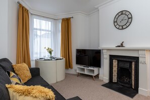 Una sala de estar con un sofá, un televisor, una chimenea y una ventana con cortinas.