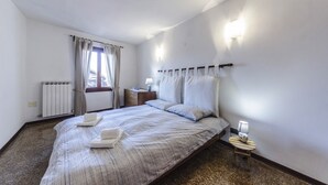 A bedroom with a bed, bedside table, lamp, and window with curtains. - Maurizio House (Venice)
