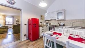 A compact kitchen with white cabinets, a red refrigerator, and a dining area with a white table set for two. - Maurizio House (Venice)