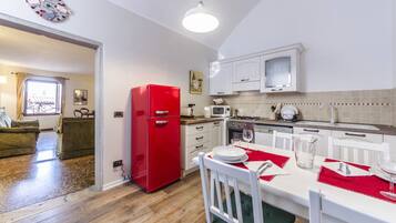 Una cocina compacta con armarios blancos, un refrigerador rojo y un comedor con una mesa blanca para dos personas.
