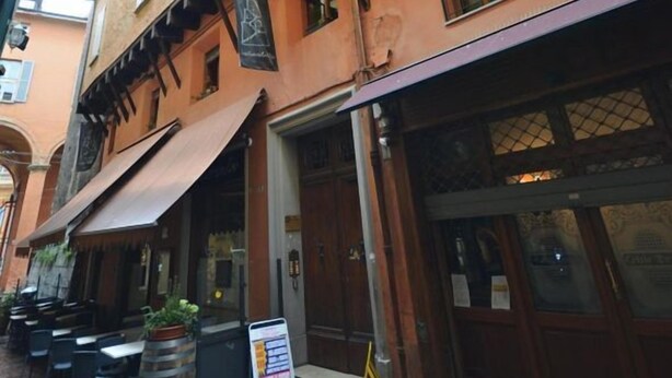 A narrow street with a building featuring a large awning, wooden doors, and a signboard. - 5 Tourist House Apartment Centre Bologna (Bologna)