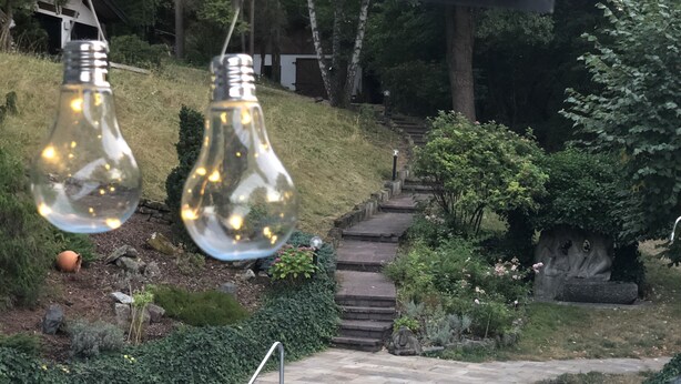 Una piscina con borde de piedra, rodeada por un jardín con escalones que conducen a una casa.
