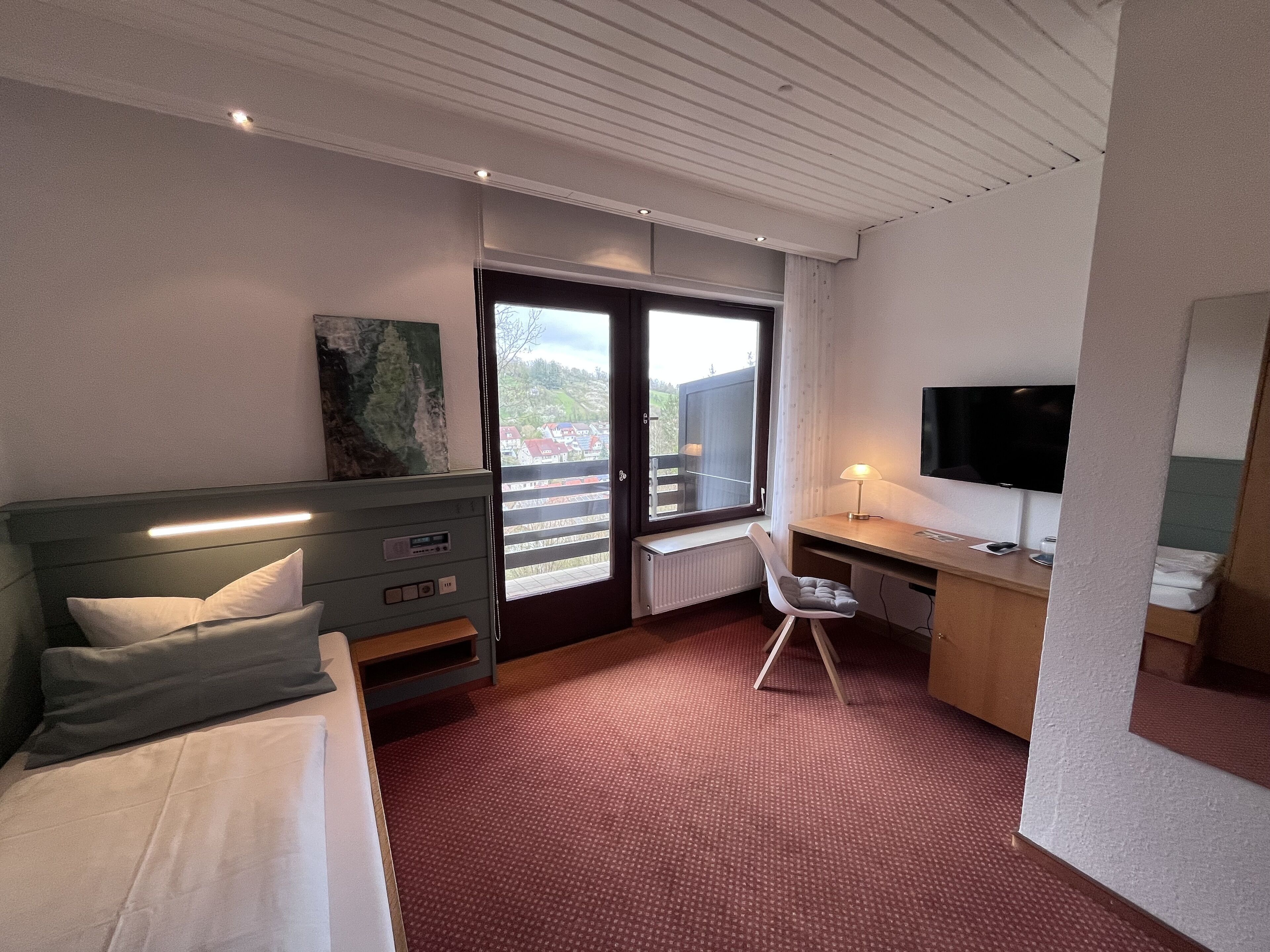 A hotel room with a bed, a desk, a chair, a TV, and a window with a view of buildings.