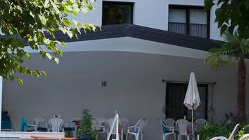 A modern building with a swimming pool, outdoor seating, and a covered patio area.
