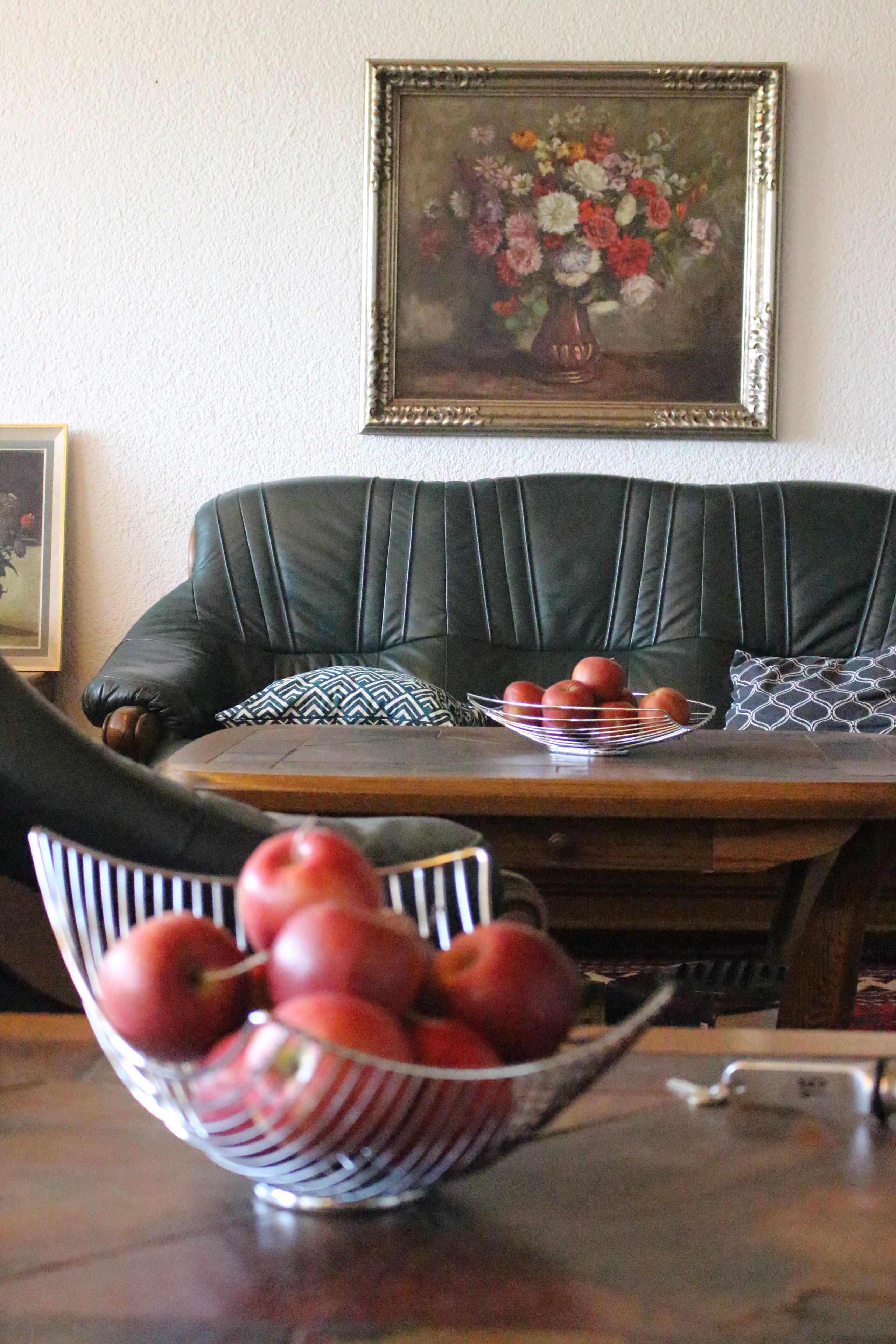 Een zithoek met een tafel, een schaal appels en een groene bekleden bank.