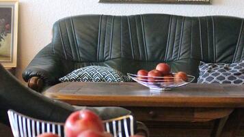 Een zithoek met een tafel, een schaal appels en een groene bekleden bank.