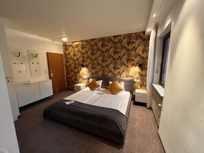 A hotel room with a large bed, two bedside tables with lamps, a wardrobe, and a patterned wallpaper. - Haus Am Wald (Eltmann)