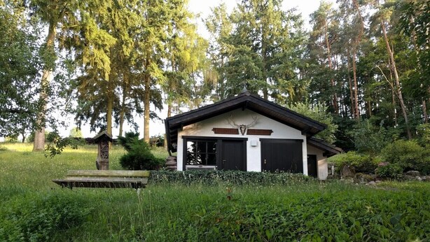 A rustic cabin with a sloped roof, a stone chimney, and a wooden porch. - Haus Am Wald (Eltmann)