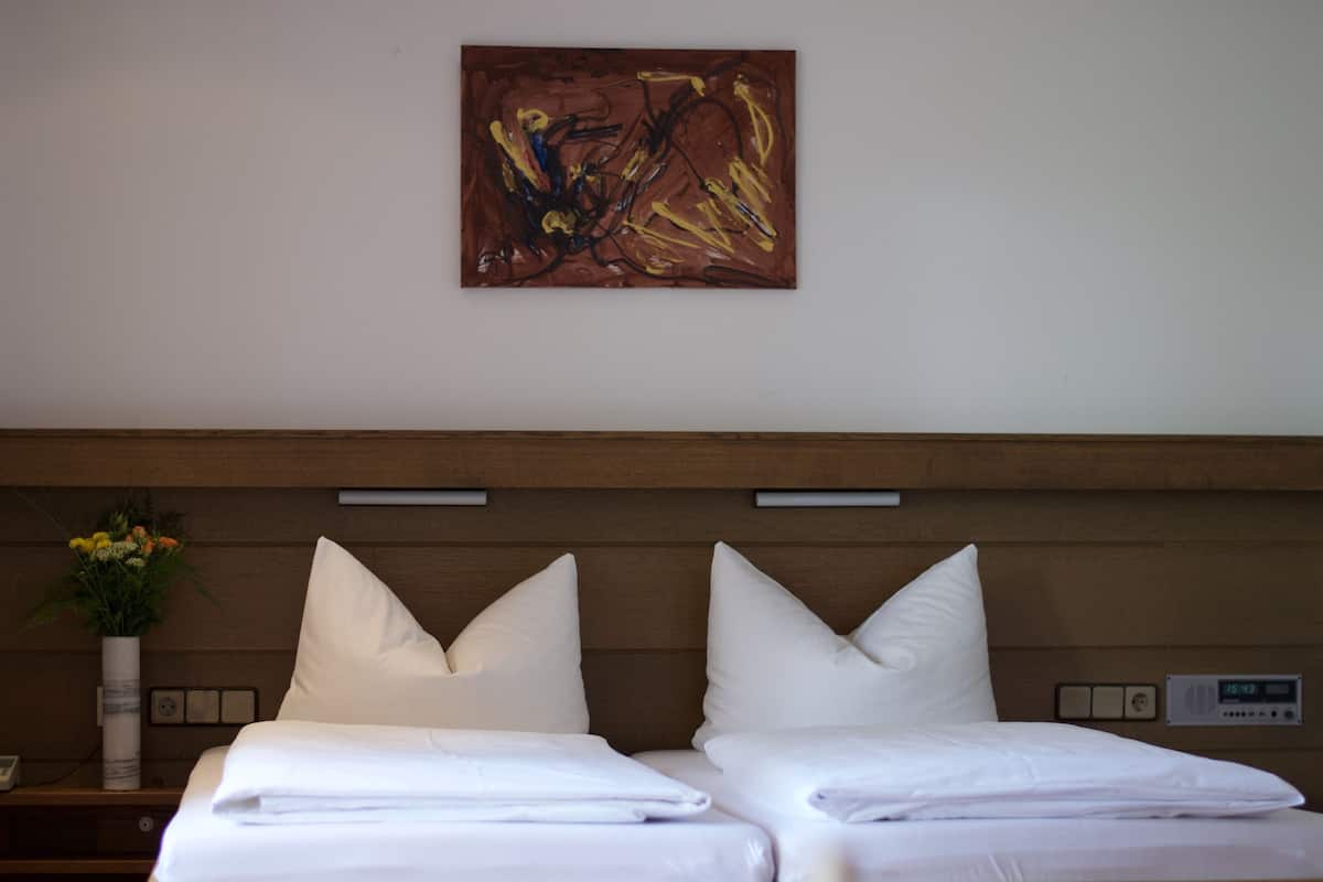 A hotel room with two beds, a wooden headboard, a painting, a vase with flowers, and a bedside table.