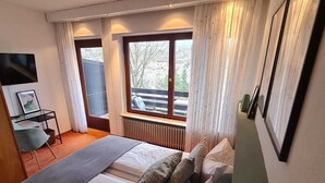A bedroom with a bed, a window, a radiator, a TV, and a chair. - Haus Am Wald (Eltmann)