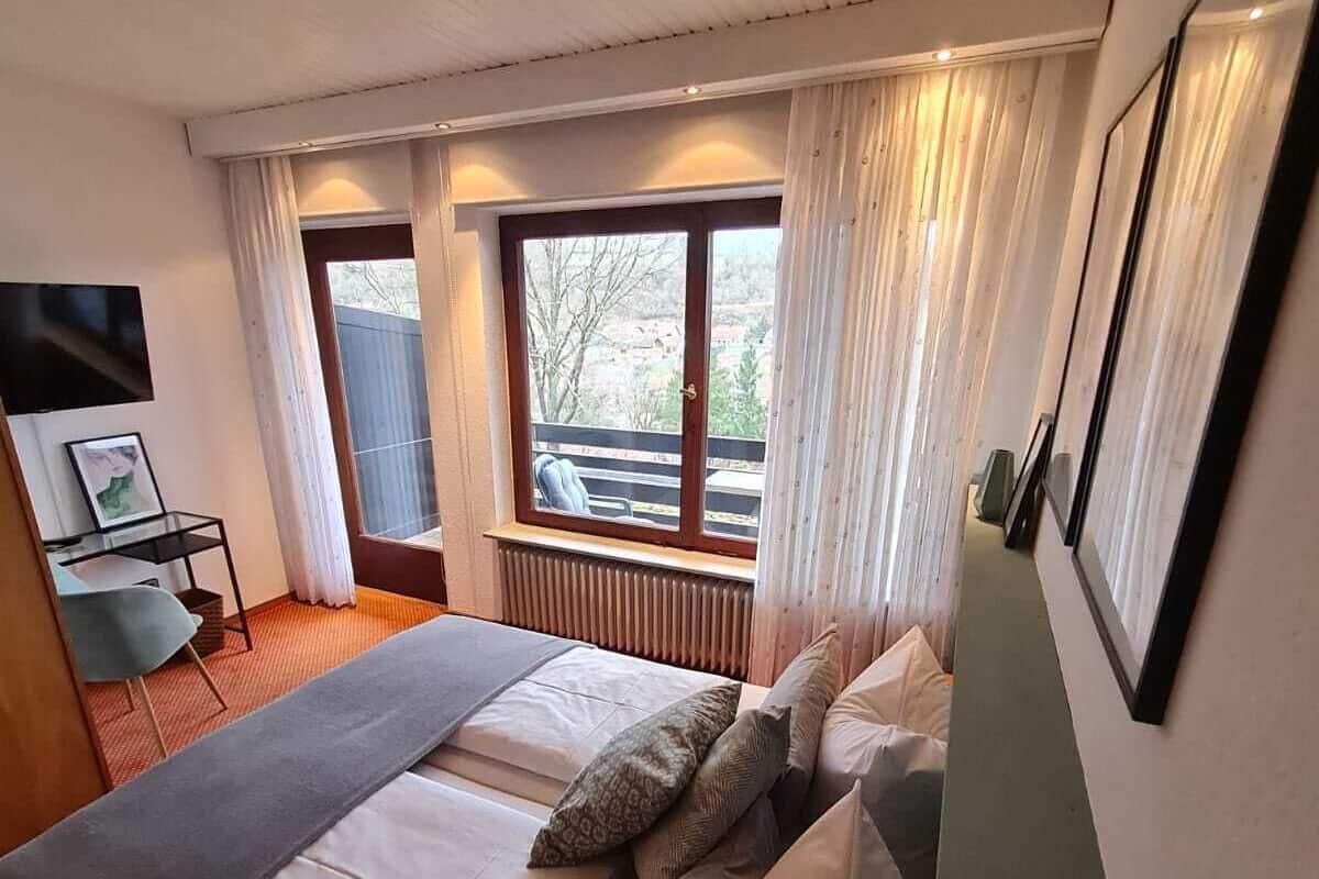 A bedroom with a bed, a window, a radiator, a TV, and a chair.