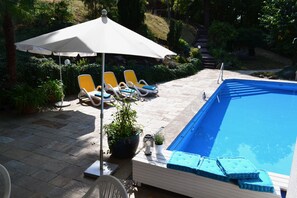 A pool area with lounge chairs, a large umbrella, and a potted plant. - Haus Am Wald (Eltmann)