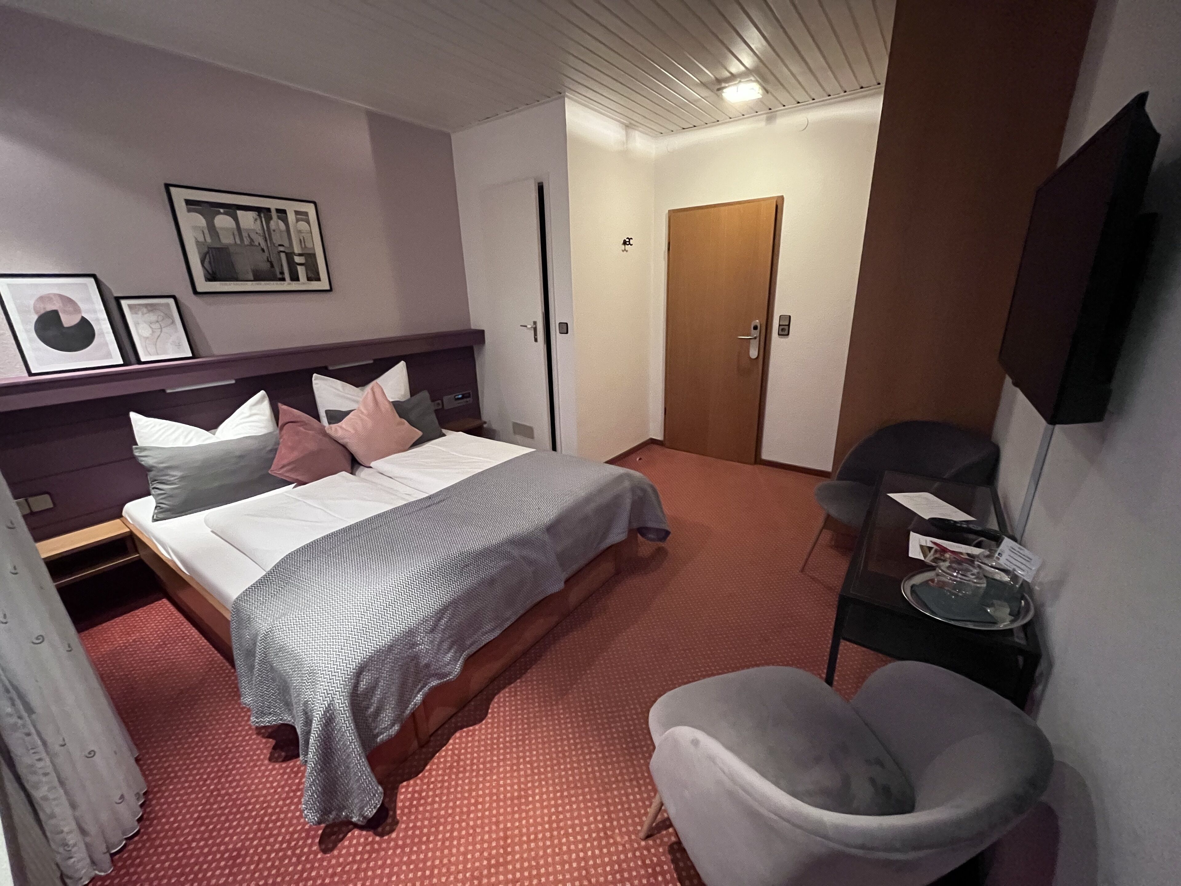 Ett hotellrum med en säng, en stol, ett skrivbord och en dörr.