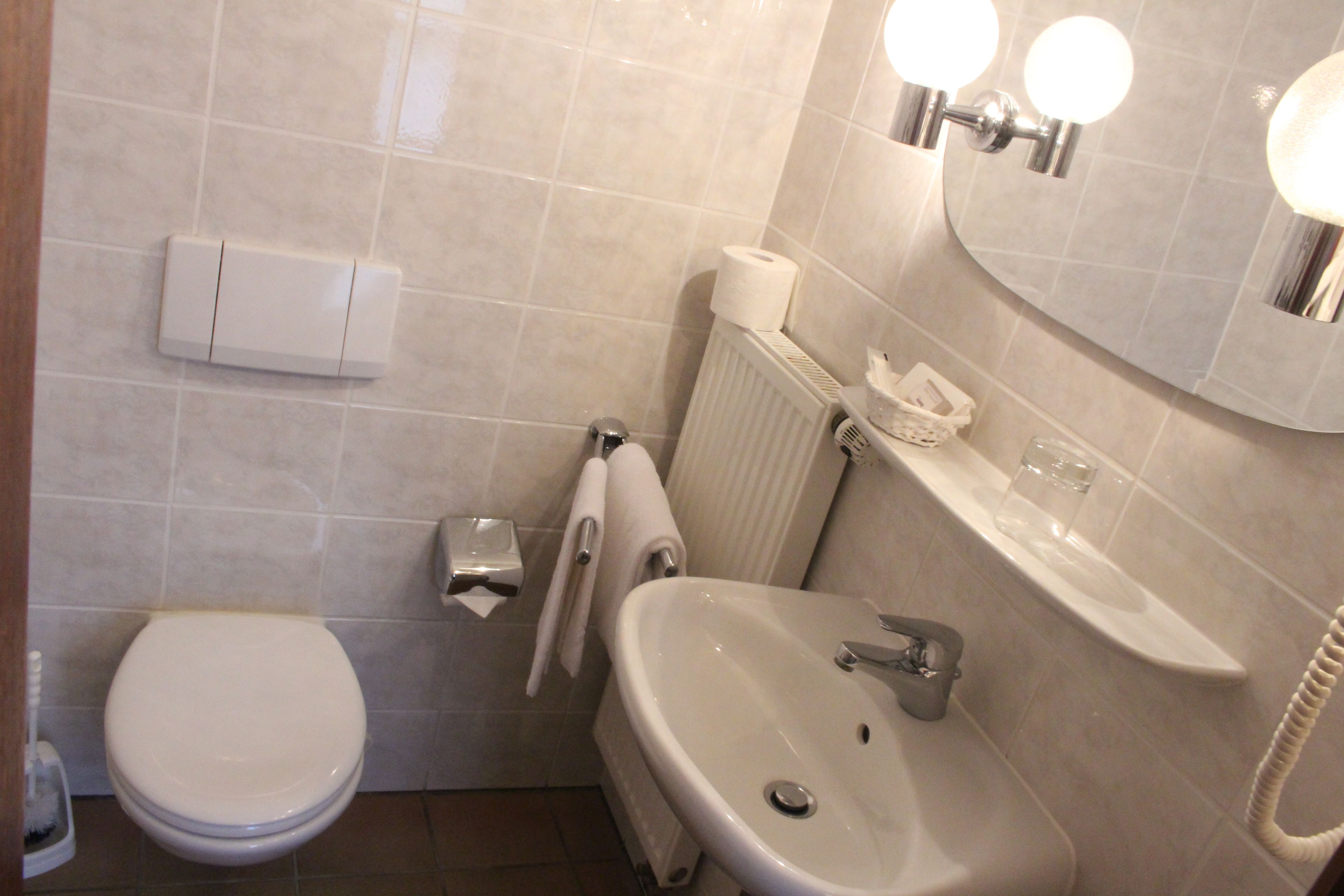 A bathroom with a toilet, sink, and mirror. There is a towel rack, a toilet paper holder, and a glass of water on the sink.