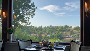 Una mesa de comedor con sillas, un florero con flores y vistas a un paisaje verde con casas.