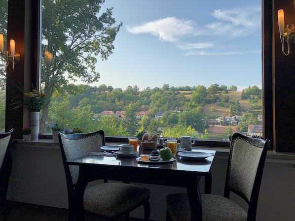 A dining table with chairs, a vase with flowers, and a view of a green landscape with houses. - Haus Am Wald (Eltmann)