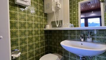 Un bagno con piastrelle verdi a motivi, un lavandino bianco, un water e un asciugamano appeso al muro.