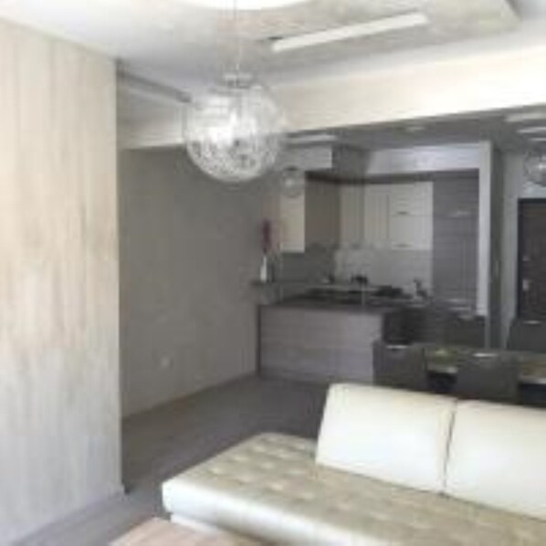 A modern living room with a sofa, a dining area with a table and chairs, and a kitchen area with cabinets and appliances. - Apartment Seaview 23 (Budva)