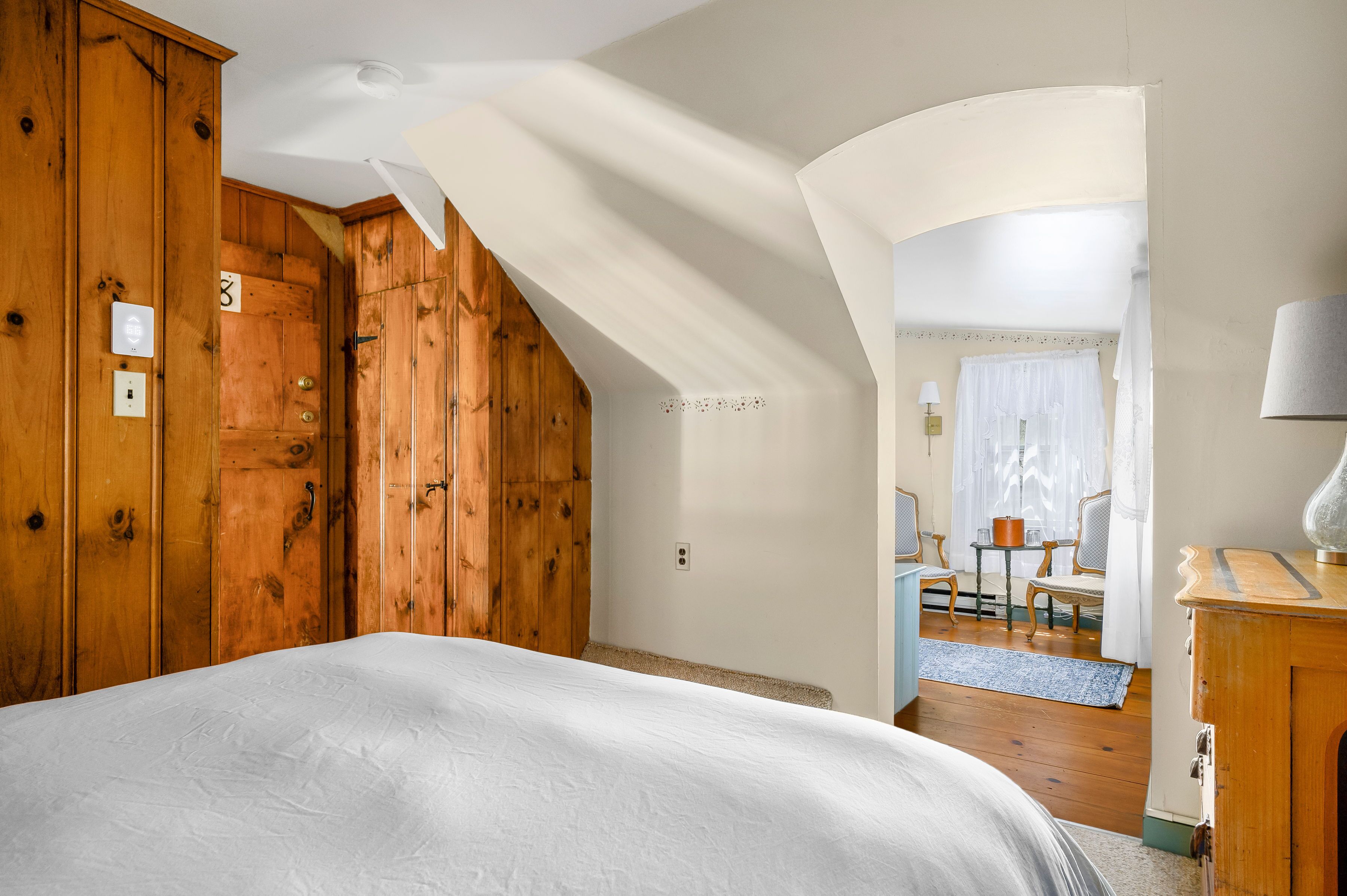 Quarto com cama grande, guarda-roupa de madeira e um pequeno espaço de estar com mesa e cadeiras.