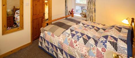 A bedroom with a large bed, a wooden wardrobe, a mirror, and a window with curtains.