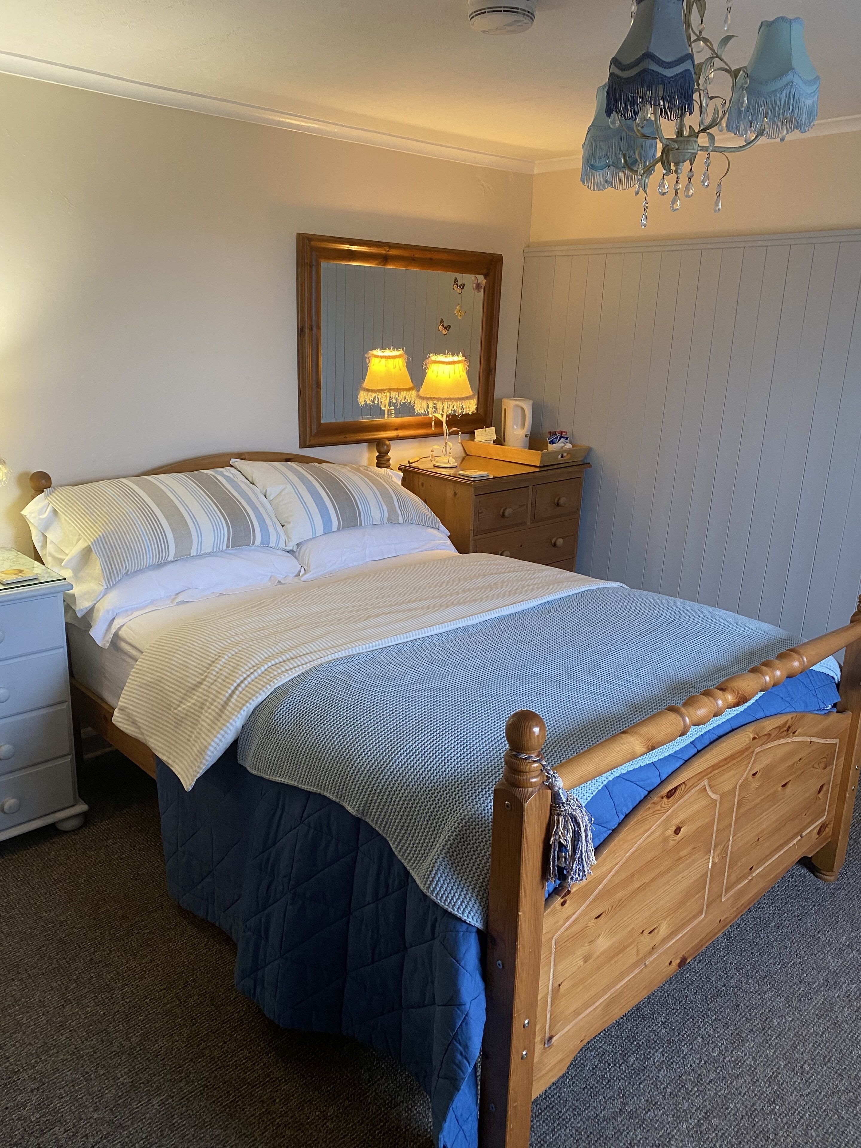 Un lit bien fait, avec une tête de lit en bois, une table de chevet avec une lampe, une commode et un miroir au mur.