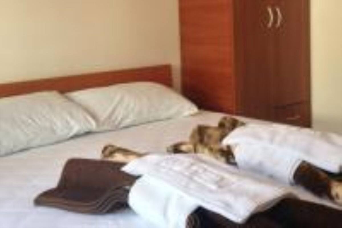 A hotel room with a bed, pillows, a wooden wardrobe, and a painting on the wall.