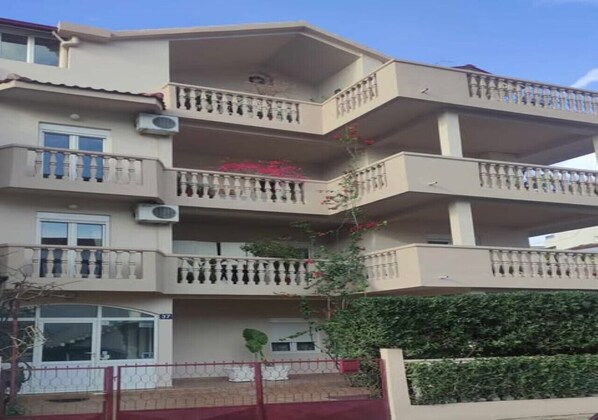 A multi-story residential building with balconies, a gated entrance, and a visible number '37' on the facade. - Rooms Kuljic (Budva)