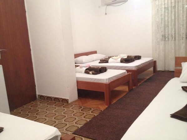 A hotel room with two beds, a wooden floor, a patterned rug, and a window with curtains. - Rooms Kuljic (Budva)