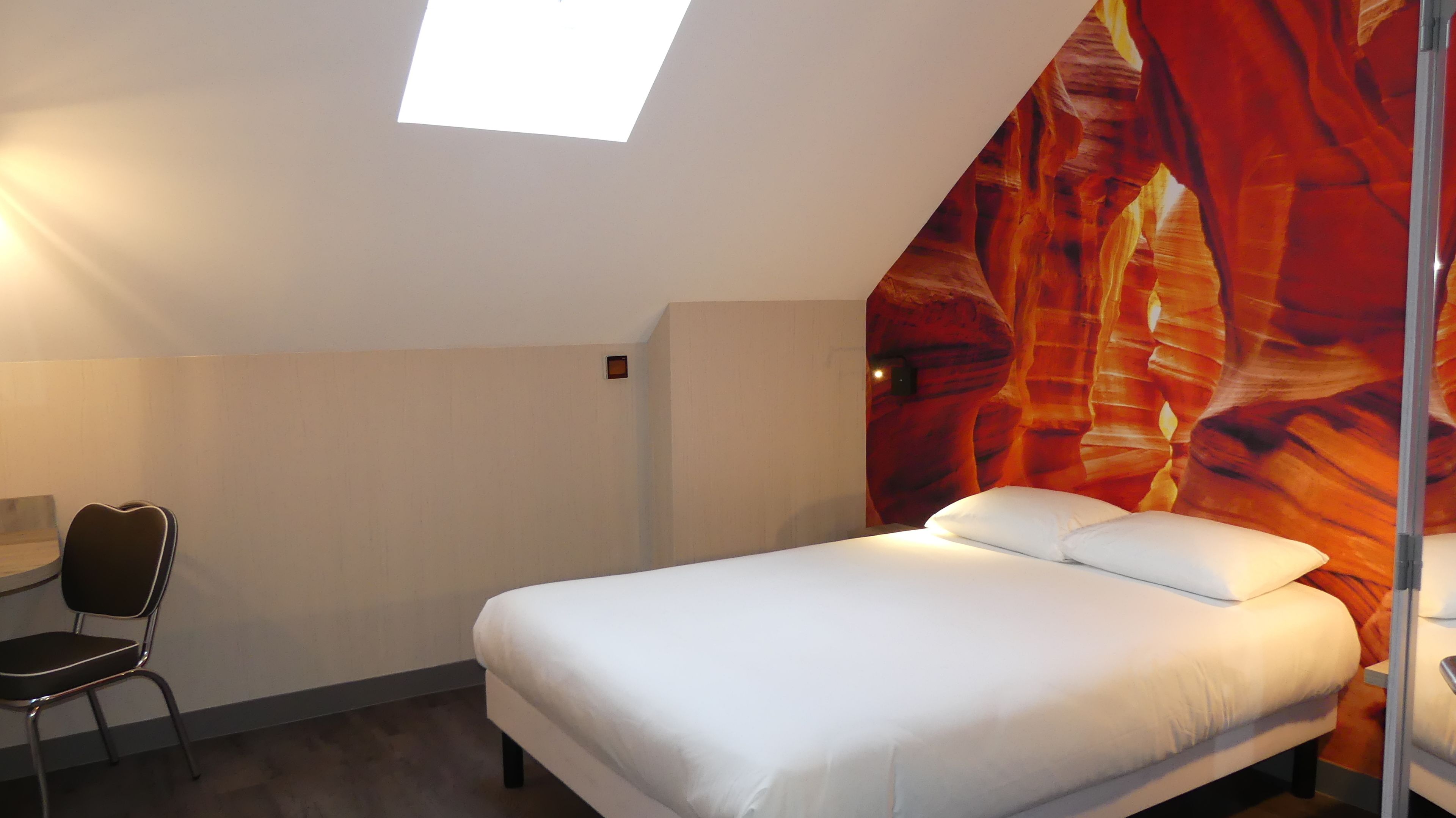 Una habitación de hotel con cama, una silla, una mesita y un ventanal grande.
