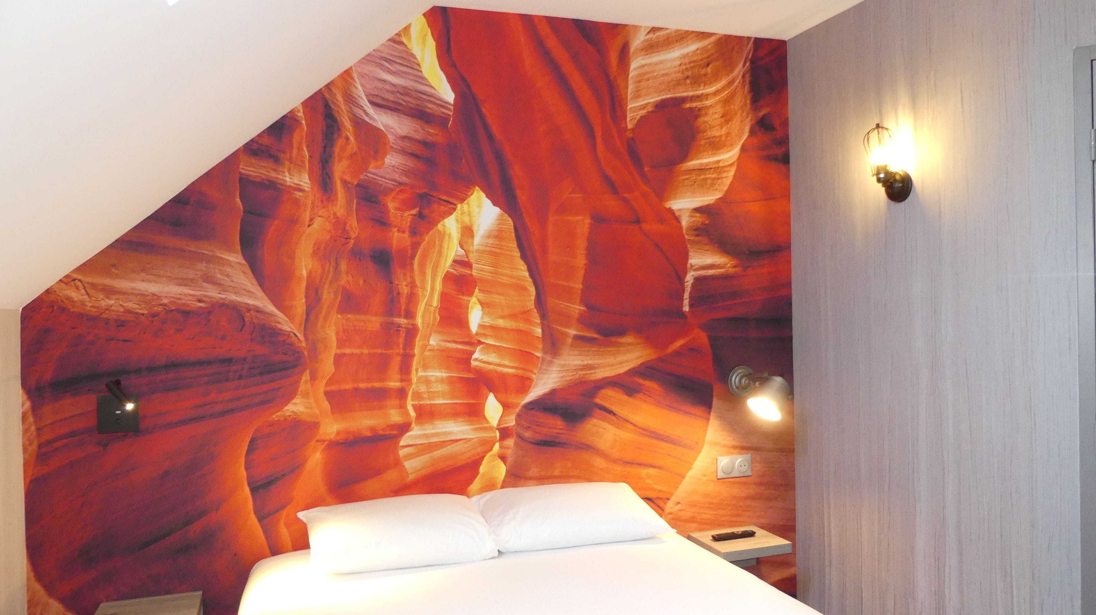 A room with a bed, a nightstand, and a wall with a rock-like mural. There are two wall-mounted lights.
