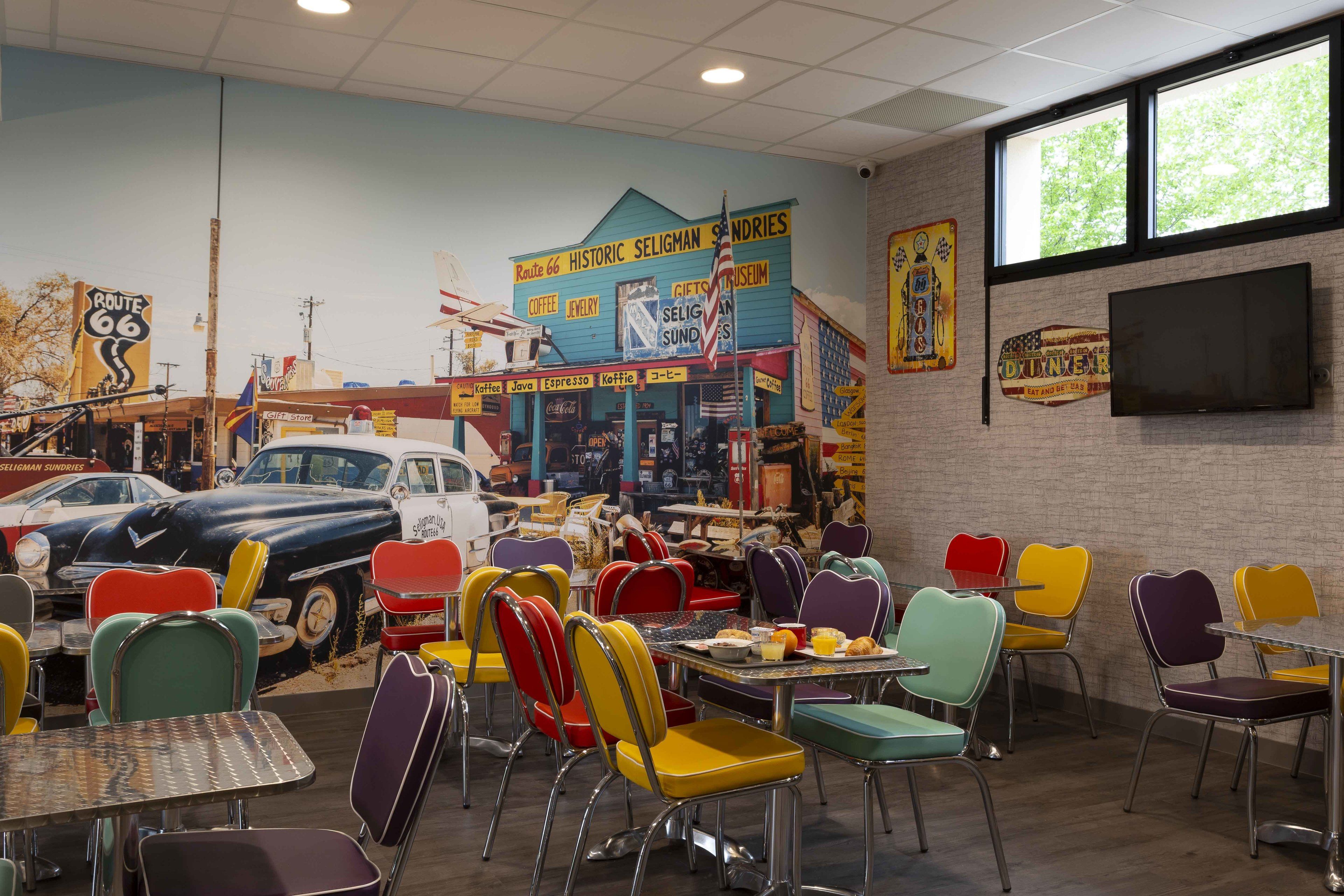 A diner with colorful chairs and tables, a Route 66 sign, and a vintage car parked outside.