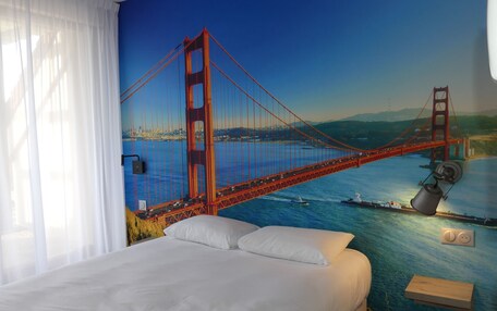 A hotel room with a large mural of the Golden Gate Bridge, a bed with white linens, and a bedside table with a lamp.