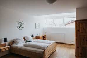 Een slaapkamer met een houten bed, een bureau, een stoel, een radiator en een raam met uitzicht op gebouwen.