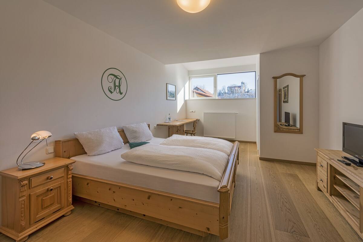 A bedroom with a wooden bed, bedside table, lamp, and a TV on a wooden stand.