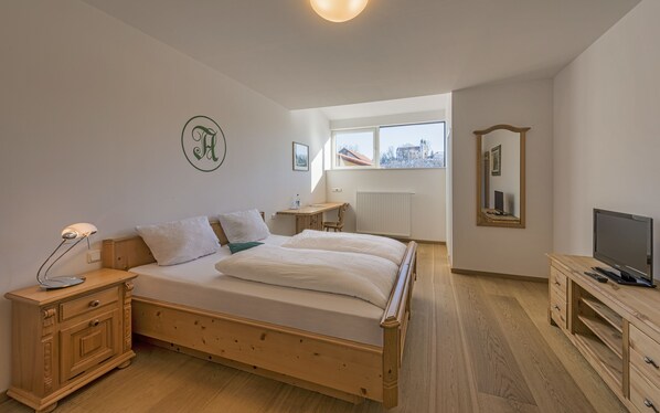A bedroom with a wooden bed, bedside table, lamp, and a TV on a wooden stand. - Angermühle Landgasthof (Altenmarkt an der Alz)