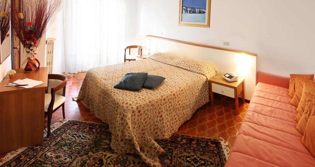 Une chambre à coucher comprenant un lit, une table de chevet, une lampe, une chaise, un bureau et un vase décoratif.